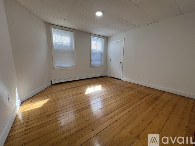 A room with wooden flooring and two windows.