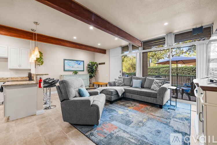 A living room with a grey couch, a grey armchair, a white cabinet, and a blue rug.