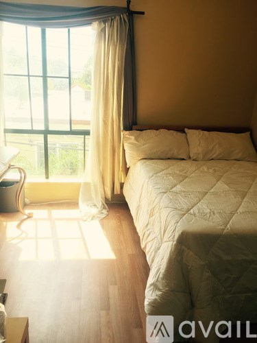 A bedroom with a bed, a window with curtains, and a chair by the window.