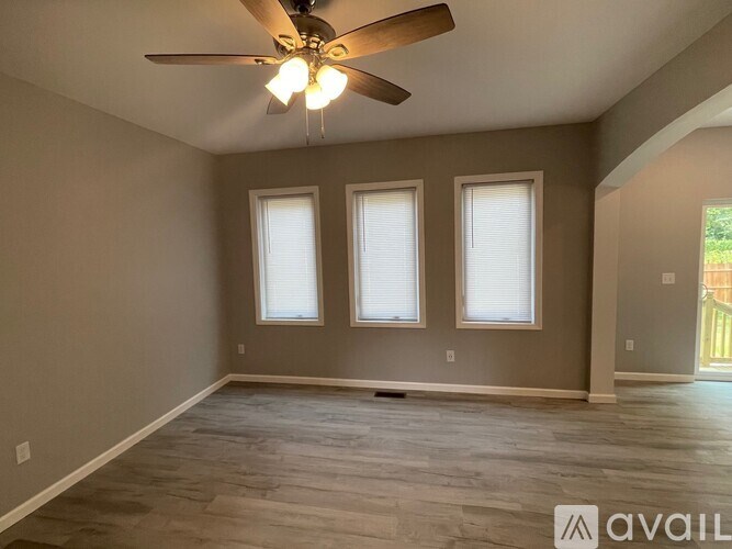 A room with a ceiling fan and three windows.