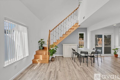 A living room with a dining table and chairs, a staircase, and a window with blinds.