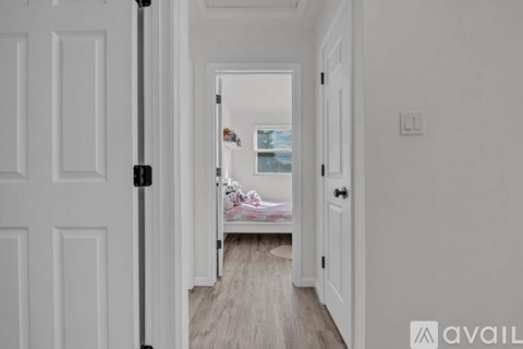 A white door opens to a room with a bed and a window.