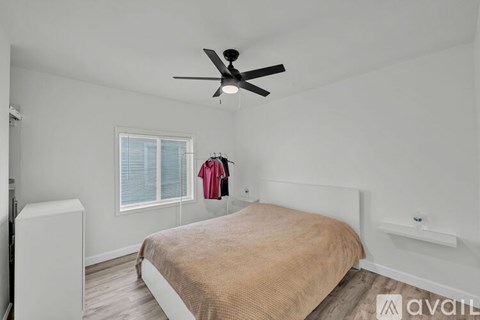 A bedroom with a bed, a ceiling fan, and a window with blinds.