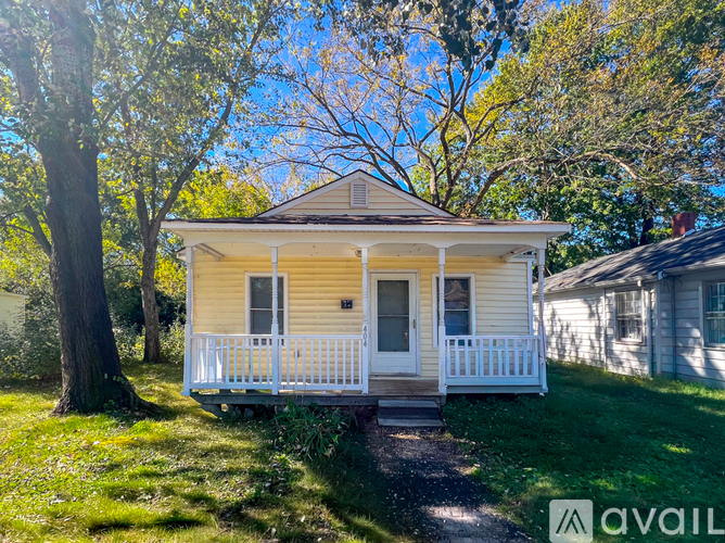 A small yellow house with a porch is surrounded by trees and grass.