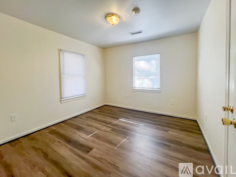 A room with wooden flooring and two windows.