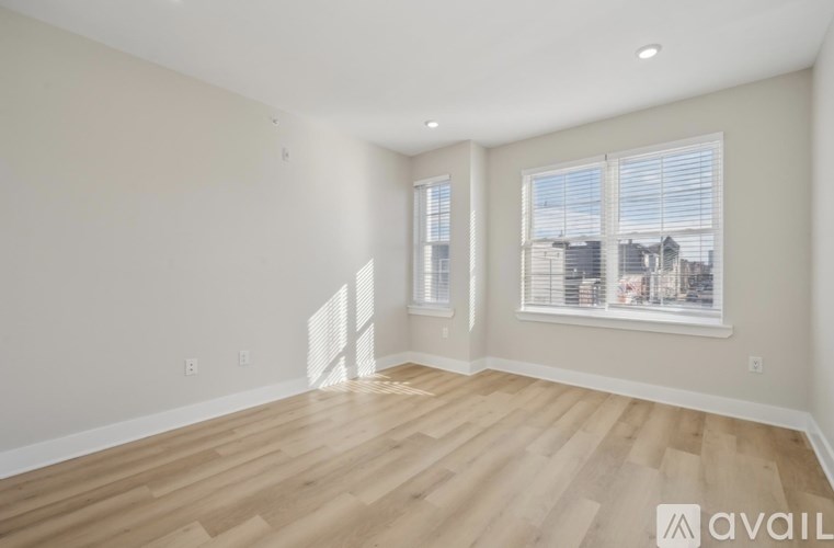 A spacious room with wooden flooring and a large window with blinds.