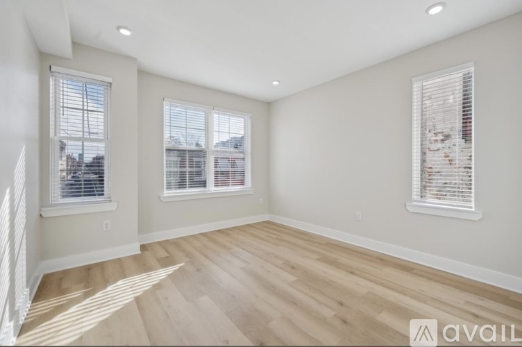 A room with wooden flooring and two windows with blinds.