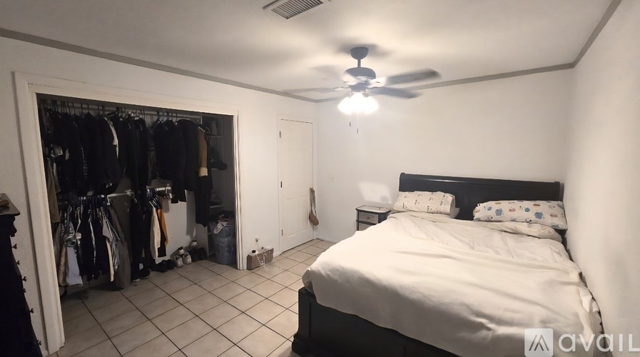 A bedroom with a bed, a ceiling fan, and a closet with clothes and bicycles.