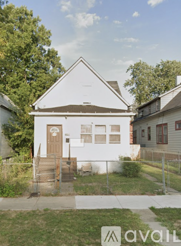 A white house with a brown door and a fence in front.