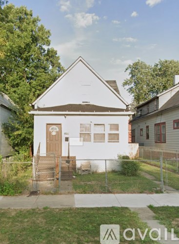 A white house with a brown door and a fence in front.
