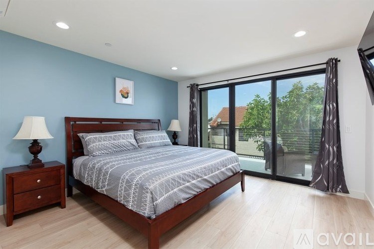 A bedroom with a large bed, a nightstand, and a sliding glass door leading to a balcony.