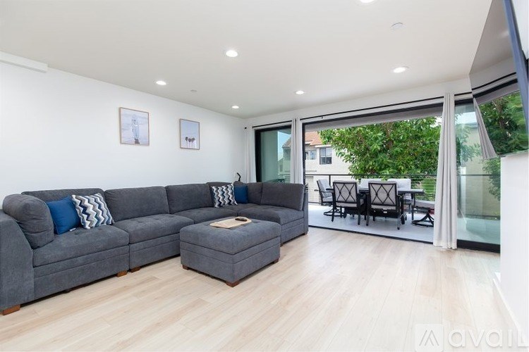 A grey sectional sofa with a small ottoman in the middle of a room with a glass table and chairs outside.