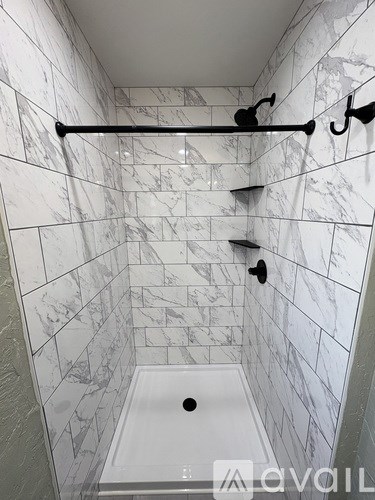 A marble tiled bathroom with a white tub and a black grab bar.
