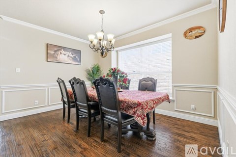 A dining room with a chandelier, a framed picture, a window with blinds, a wooden floor, and a table with chairs.