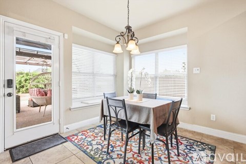 A dining room with a table set for two and a view of a backyard through the window.