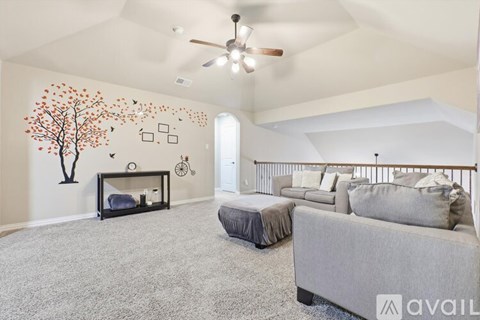 A living room with a grey couch, a grey ottoman, a fireplace, and a tree mural on the wall.