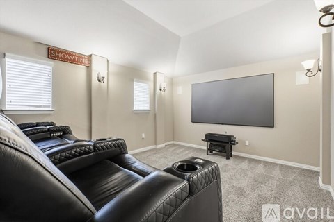A living room with a black leather couch and a flat screen TV mounted on the wall.