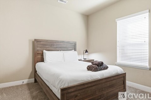A bed with a wooden headboard and white bedding is in a room with a window on the right.