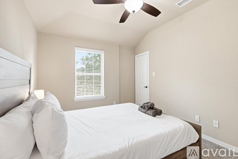 A bedroom with a bed, pillows, a window with blinds, a ceiling fan, and a door.