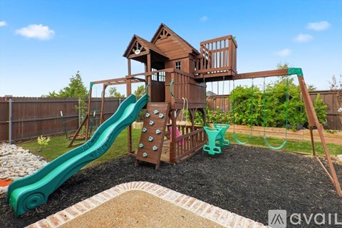 A wooden playset with a green slide in a backyard.