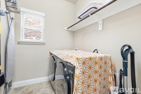 A laundry room with a washer and dryer, a window with blinds, and a vacuum cleaner.