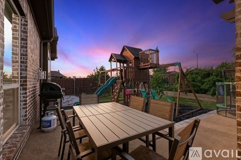 A wooden table and chairs are set up on a patio with a playground in the background.