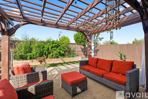 A patio with a red couch and a wooden pergola.
