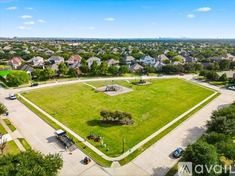 A large grassy park with a playground and a few cars parked on the street.