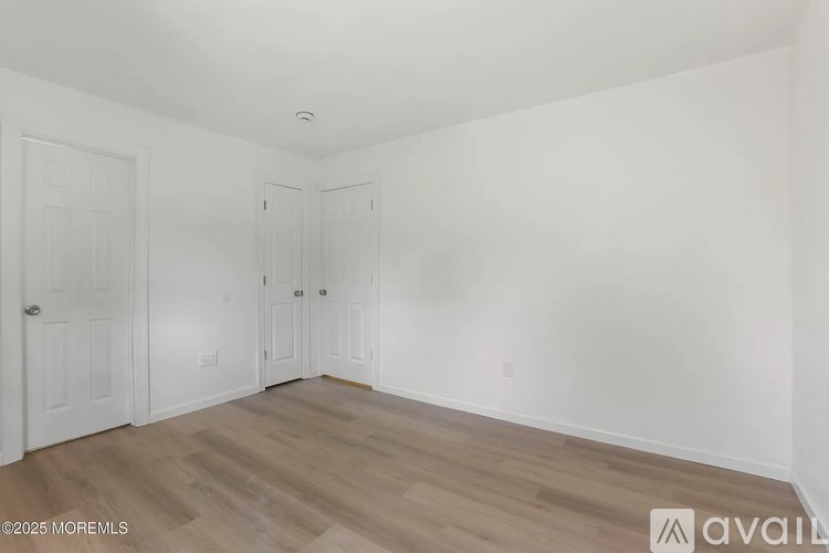 A room with white walls and wooden flooring, with three doors and a ceiling light fixture.