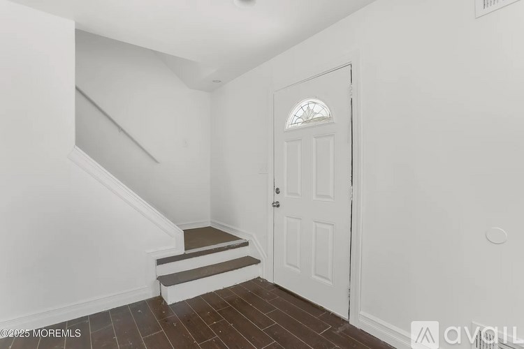 A white door with a window in the middle is in a room with white walls and a staircase.