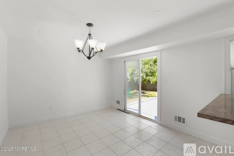 A large empty room with a chandelier and a sliding glass door leading to a patio.