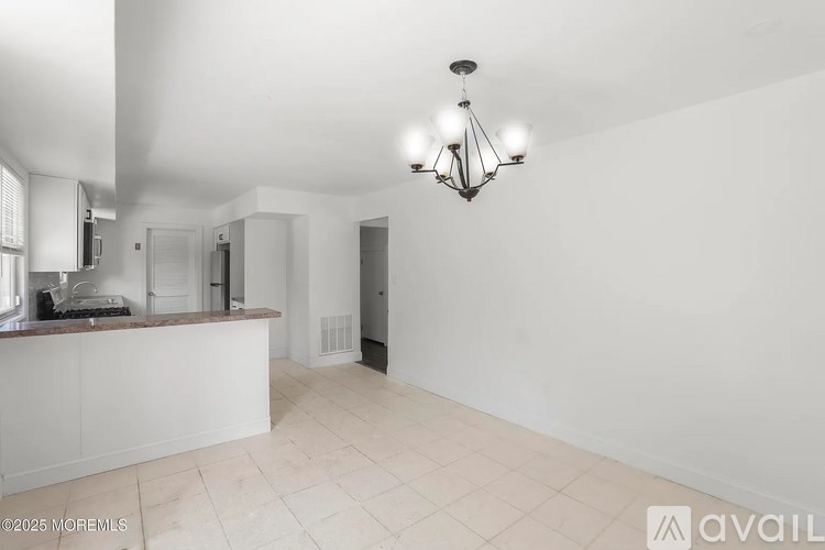A large, empty room with a kitchen area and a chandelier.