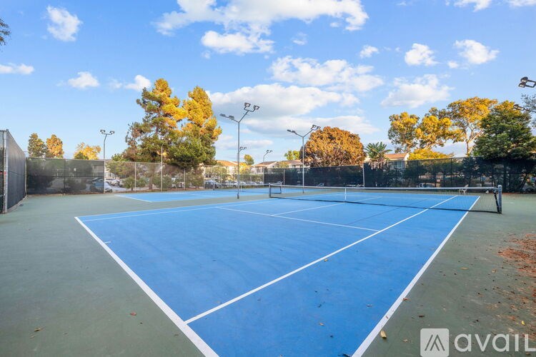 A tennis court with a blue surface and white lines, surrounded by trees and a fence.