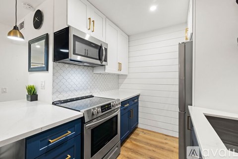 A kitchen with a black microwave above a stove and blue cabinets.