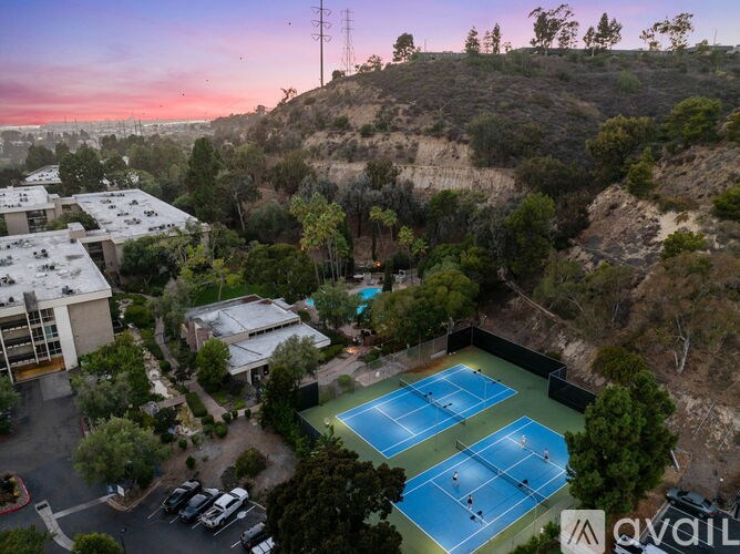 Two tennis courts are surrounded by trees and houses.