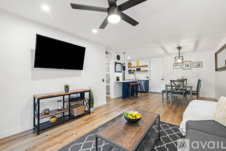 A living room with a ceiling fan and a flat screen TV mounted on the wall.