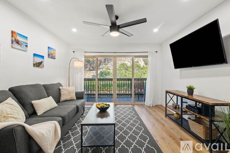 A living room with a grey sofa, a black coffee table, a ceiling fan, and a flat screen TV mounted on the wall.