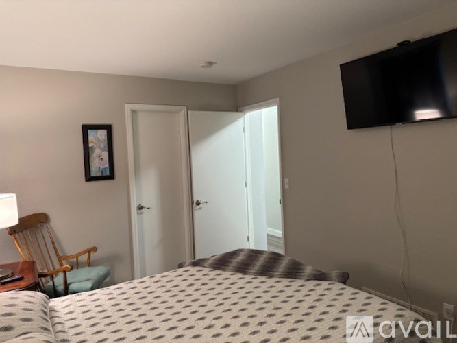 A bedroom with a bed, a chair, a lamp, and a flat-screen TV mounted on the wall.