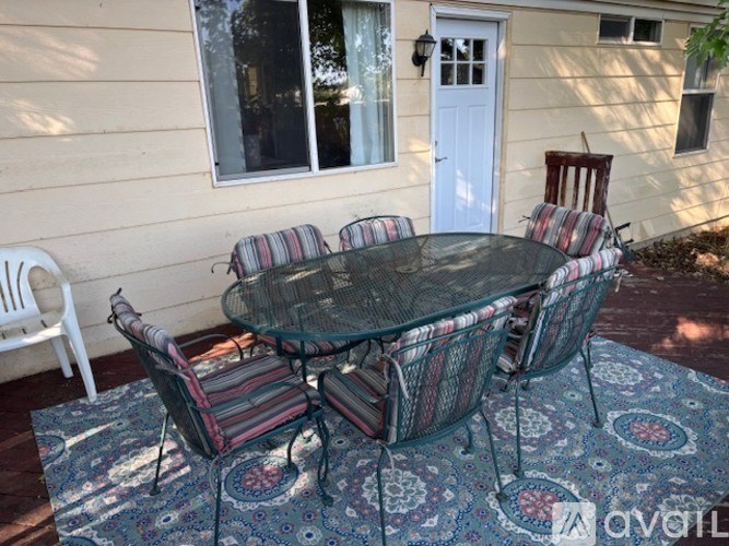 A glass table with four chairs and a rug in front of a house.