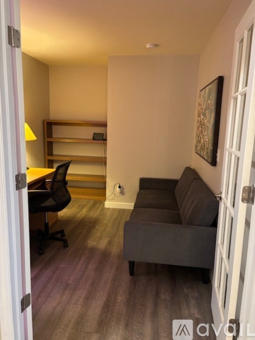 A room with a grey couch, a black chair, and a wooden shelf with a lamp.