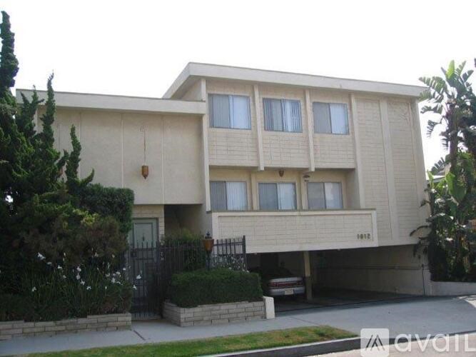 A beige two-story house with a black gate and bushes in front.