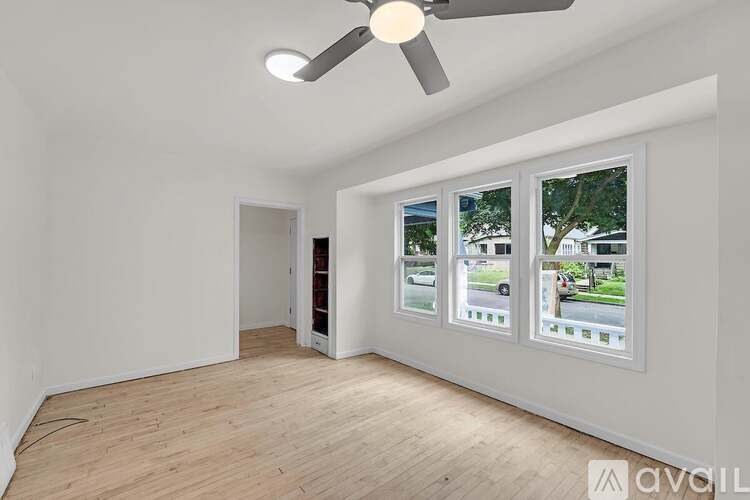 A room with a ceiling fan and three windows showing the outside view.