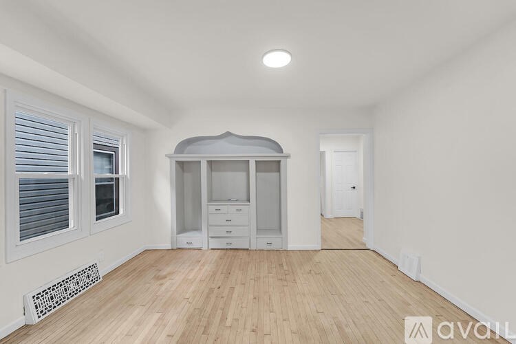 A room with wooden flooring, a window with blinds, a white cabinet, and a radiator.