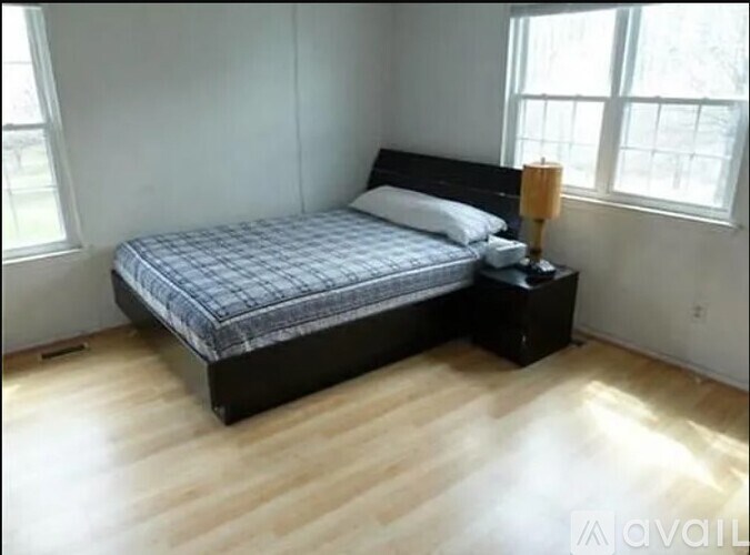 A bed with a black headboard and a grey bedspread is in a room with wooden flooring and white walls.