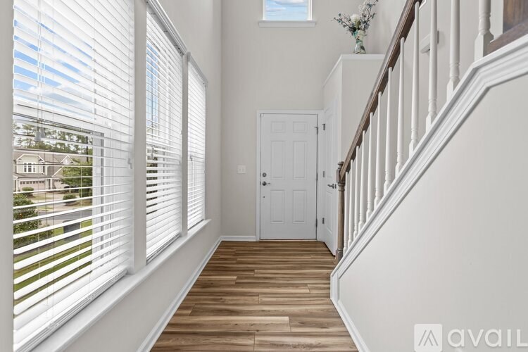 A hallway with a wooden floor and white walls leading to a white door.