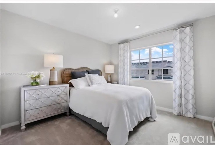 A bedroom with a white bed and a window with curtains.