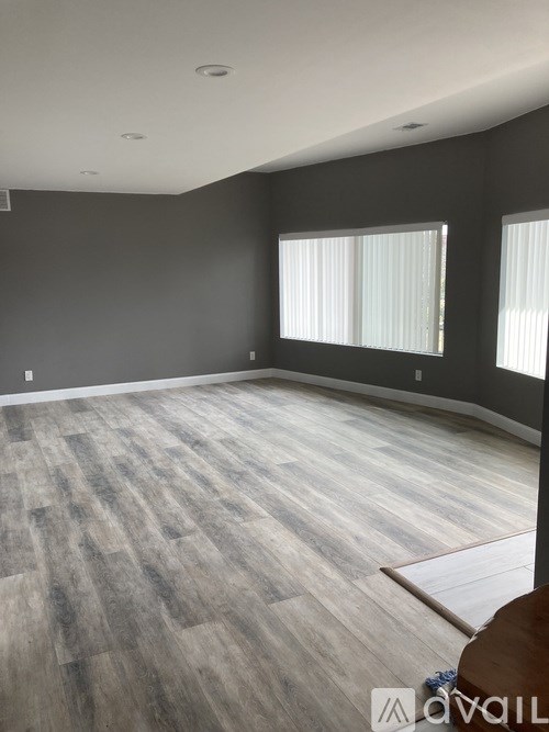 A room with wooden flooring and two windows.