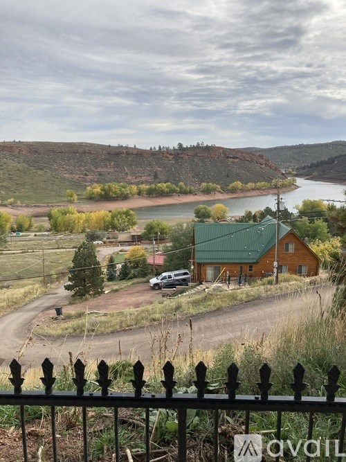 A house with a green roof is surrounded by a fence and a river can be seen in the background.