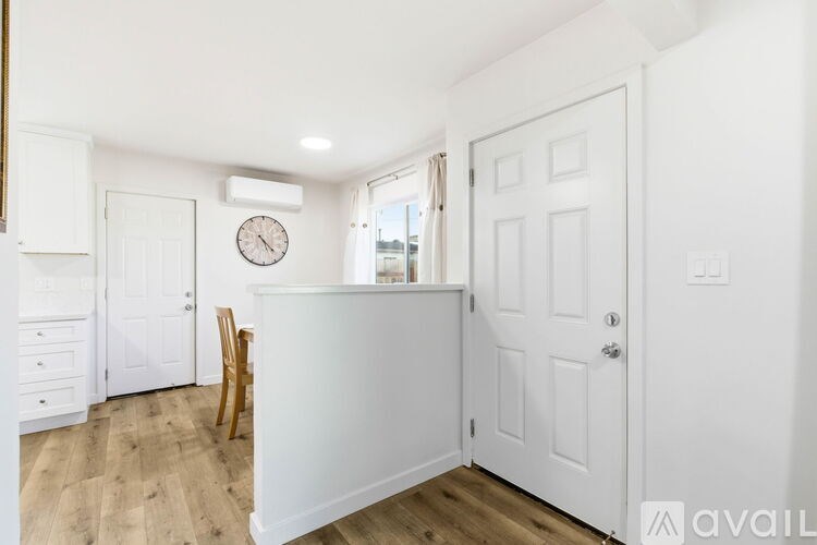 A white kitchen with a wooden floor and a clock on the wall.