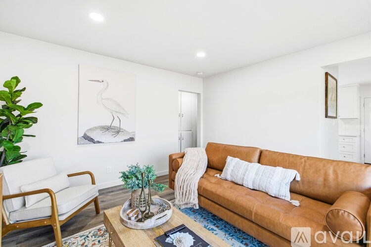 A living room with a brown leather couch, a white chair, and a painting of a white bird on the wall.